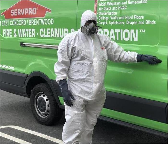 A person wearing protective gear in front a green van SERVPRO van 